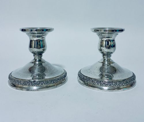 fig 1. A pair of short sterling silver desk candlesticks featuring round bases with chased floral borders and baluster stems.