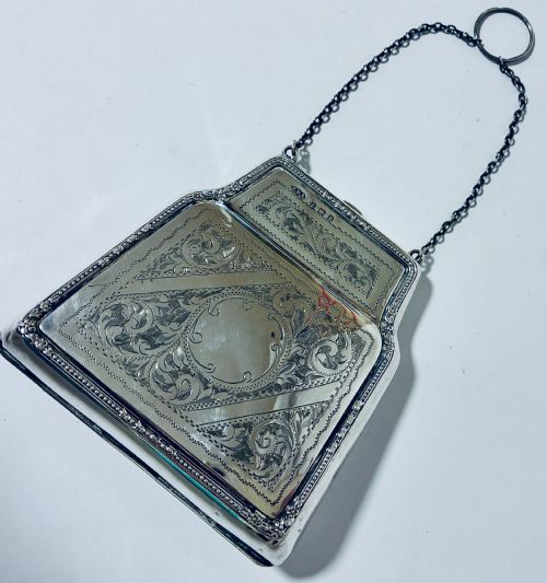 fig 1. An antique sterling silver evening purse featuring engraved floral scrollwork, visible hallmarks along the upper frame, and a chain handle with a finger ring.