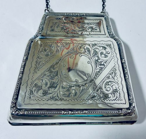 fig 2. An antique sterling silver evening purse featuring engraved floral scrollwork, visible hallmarks along the upper frame, and a chain handle with a finger ring.