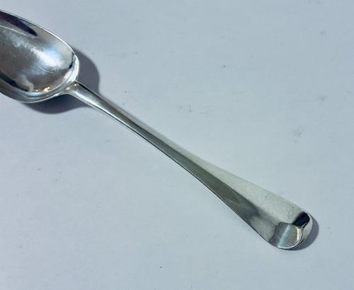 fig 2. An 18th-century sterling silver serving spoon with a wide oval bowl and a smooth stem handle resting on a plain background.