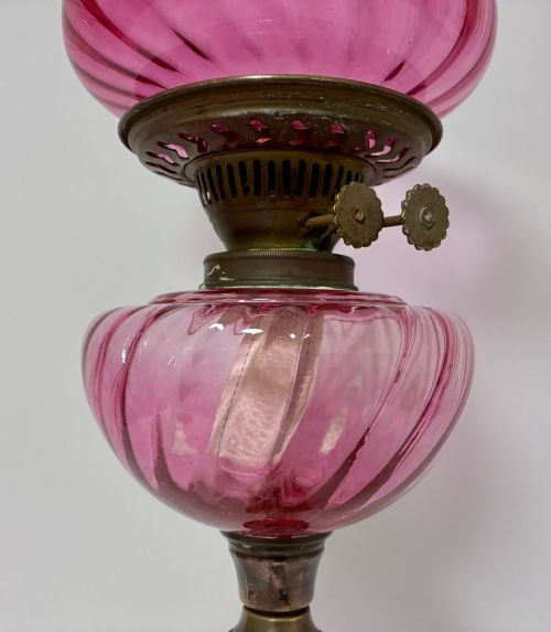 fig 1. A Victorian oil lamp featuring a swirl optique cranberry glass shade and reservoir set atop a brass column and relief-moulded square base.
