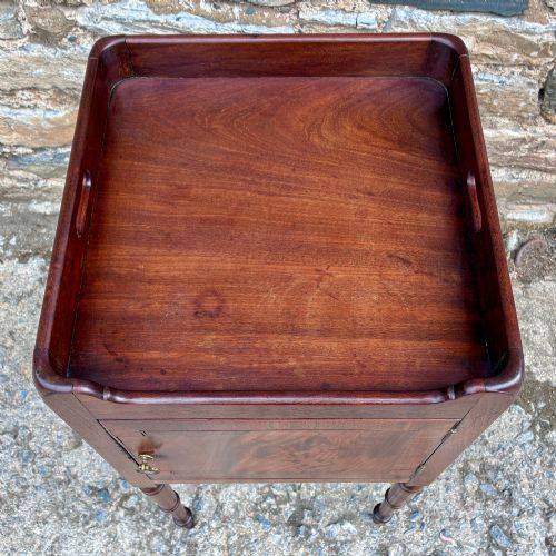 fig 1. A Georgian mahogany pot cupboard featuring a tray top gallery with cut-out handles, a single veneered door, and turned legs.