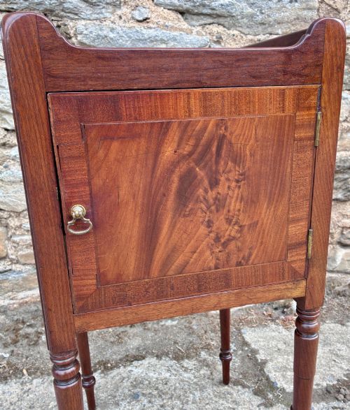 fig 2. A Georgian mahogany pot cupboard featuring a tray top gallery with cut-out handles, a single veneered door, and turned legs.