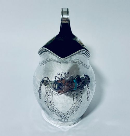 fig 2. A Georgian sterling silver cream jug featuring a high loop handle, poured spout, and bright-cut star motif engraving on its body.