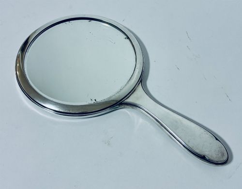 fig 1. An antique oval silver hand mirror resting horizontally against a plain background.