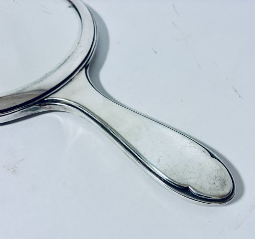 fig 2. An antique oval silver hand mirror resting horizontally against a plain background.