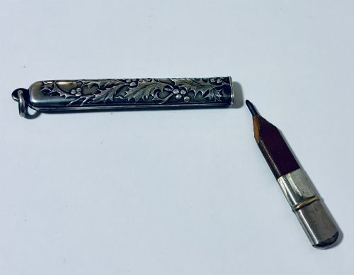 fig 1. An antique silver cylindrical pencil holder featuring repousse holly leaf and berry decoration with a suspension ring attached to the end.