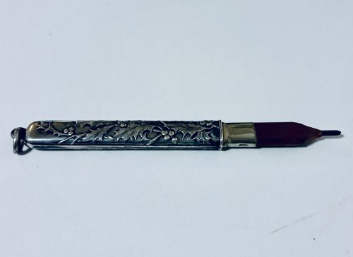 fig 2. An antique silver cylindrical pencil holder featuring repousse holly leaf and berry decoration with a suspension ring attached to the end.