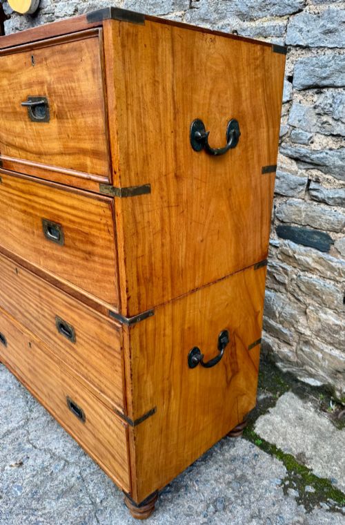 fig 2. A Victorian camphor wood military campaign chest of drawers featuring two short over three long drawers with flush brass handles, corner straps, and turned feet.
