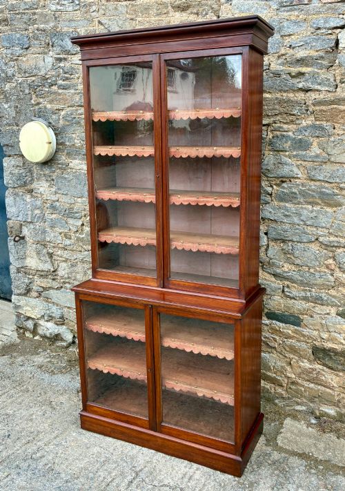 fig 3. A tall Victorian mahogany cabinet featuring an upper two-door glazed section with scalloped shelf edging set above a lower matching glazed cupboard.
