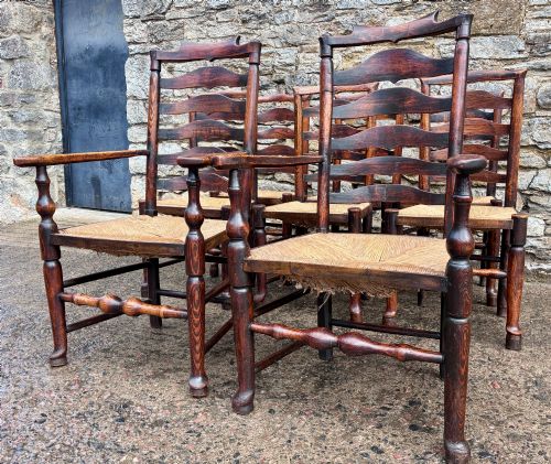 fig 2. A set of eight 19th-century dark timber Lancashire ladderback dining chairs featuring wavy back slats, turned front stretchers, and woven rush seats, comprising two carver armchairs and six side chairs.