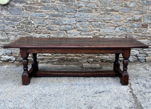 fig 1. A long dark oak refectory dining table featuring a solid plank top, cleated ends, turned legs, and a low stretcher rail.