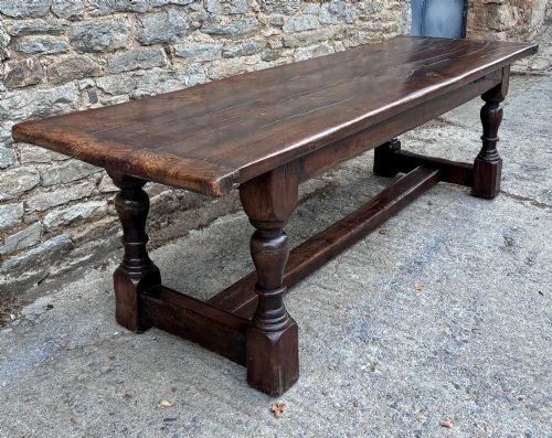 fig 2. A long dark oak refectory dining table featuring a solid plank top, cleated ends, turned legs, and a low stretcher rail.