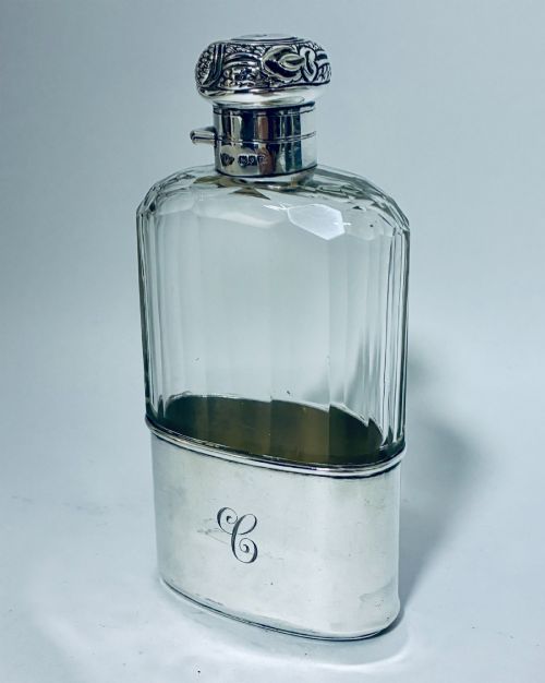 fig 1. An antique cut-glass hip flask featuring a hallmarked sterling silver collar, chased cap, and a removable silver base cup engraved with the letter C.