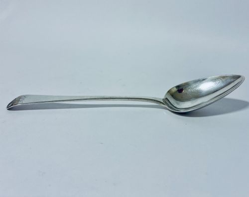 fig 1. A Georgian sterling silver serving spoon featuring an Old English pattern stem with an engraved crest and a tapered oval bowl against a white backdrop.