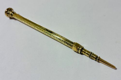 fig 1. An antique gold propelling pencil featuring detailed scroll engraving along its slender hexagonal barrel and a polished tip.