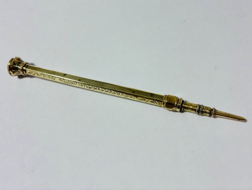 fig 2. An antique gold propelling pencil featuring detailed scroll engraving along its slender hexagonal barrel and a polished tip.