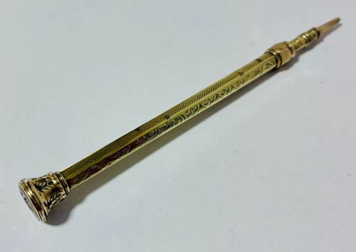 fig 3. An antique gold propelling pencil featuring detailed scroll engraving along its slender hexagonal barrel and a polished tip.