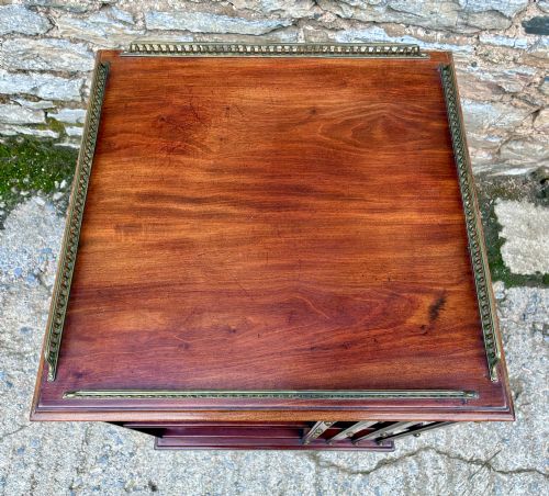 fig 2. An Edwardian mahogany revolving bookcase featuring a square top with a brass gallery rail, slatted sides with brass studs, two tiers of shelving, and a central rotating mechanism on castors.