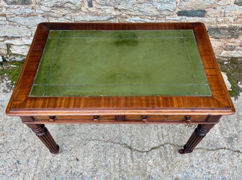 fig 2. A Victorian mahogany writing table featuring a green leather top, two front drawers with turned wooden knobs, and fluted turned legs on brass castors.