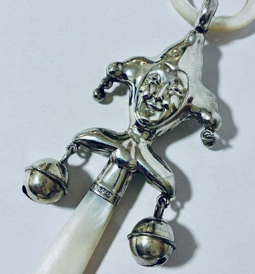 fig 1. An antique sterling silver baby rattle shaped like a jester with hanging bells, a mother-of-pearl handle, and an attached ring.