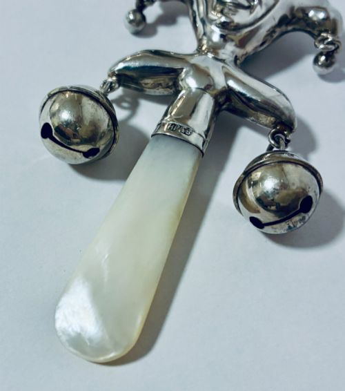 fig 2. An antique sterling silver baby rattle shaped like a jester with hanging bells, a mother-of-pearl handle, and an attached ring.