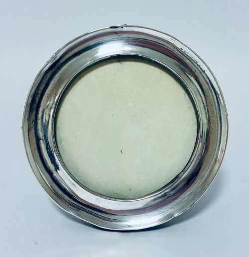fig 1. A circular antique silver photo frame with a raised convex moulding rim and a black easel backing.