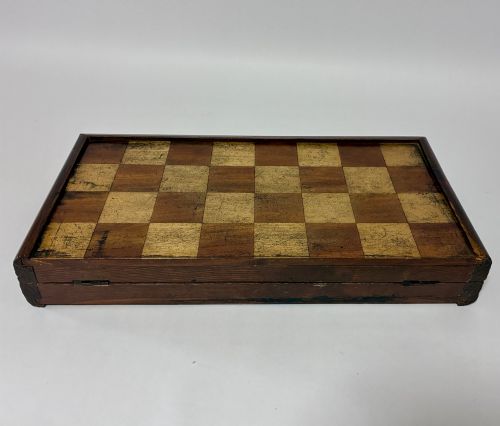 fig 2. An antique hinged wooden folding games board with a checkerboard surface, accompanied by turned draughts counters and a sliding wooden box containing chess pieces.