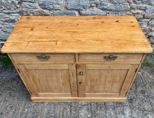 fig 1. A nineteenth-century stripped pine sideboard featuring two upper drawers with ornate brass handles above two panelled cupboard doors on a solid plinth base.