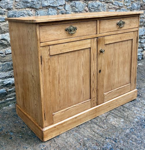 fig 2. A nineteenth-century stripped pine sideboard featuring two upper drawers with ornate brass handles above two panelled cupboard doors on a solid plinth base.