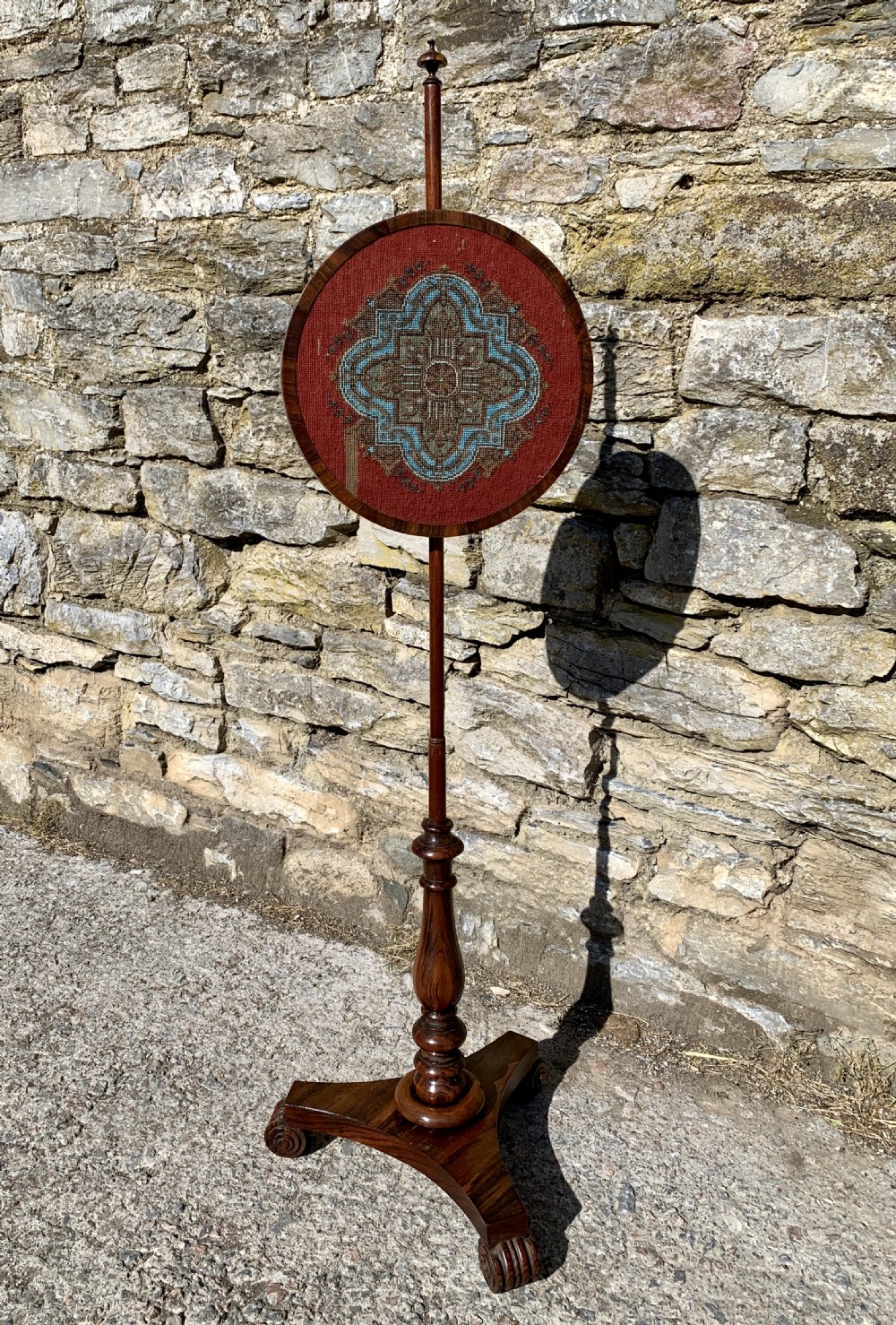 A Regency rosewood pole screen with a circular needlepoint panel on a turned column and triform base. View II