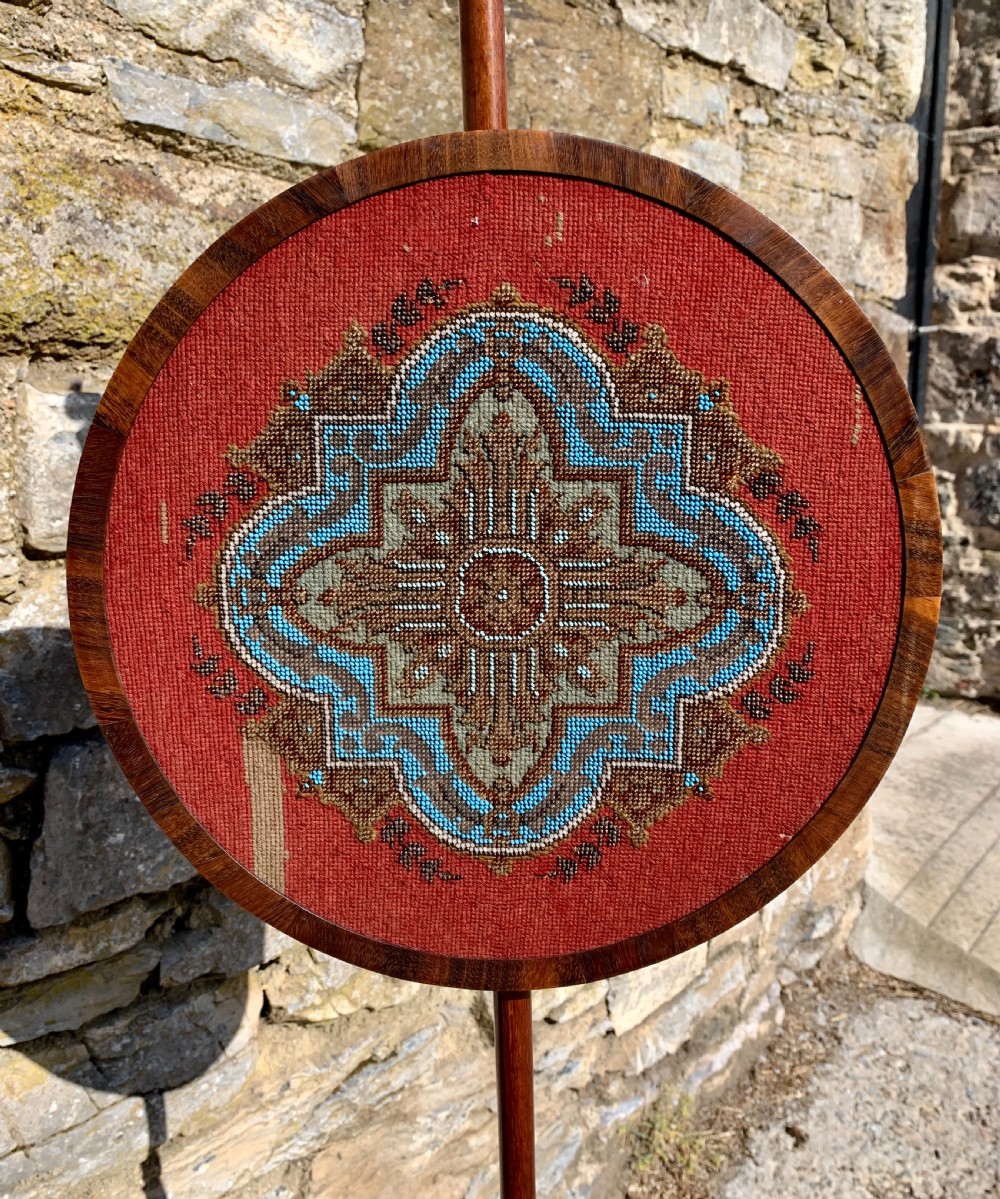 A Regency rosewood pole screen with a circular needlepoint panel on a turned column and triform base. View VII