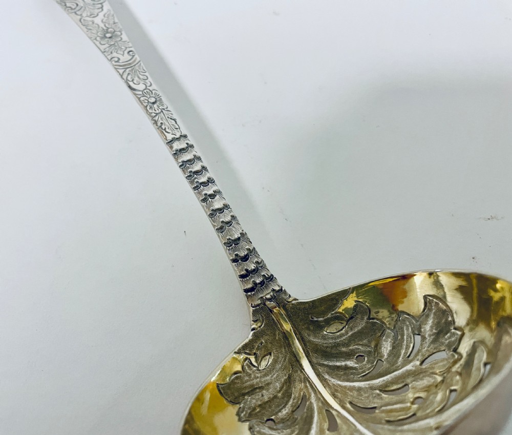 A Georgian sterling silver sugar sifter spoon featuring a hand-pierced foliate bowl design and an engraved floral handle. View V