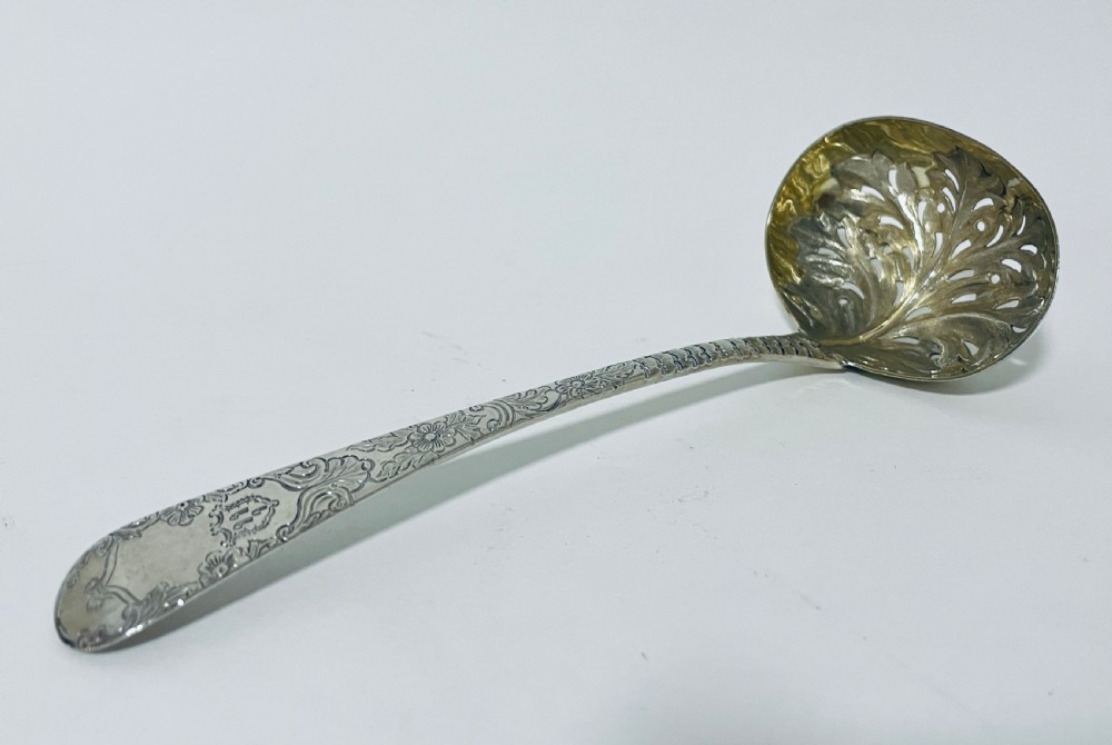 A Georgian sterling silver sugar sifter spoon featuring a hand-pierced foliate bowl design and an engraved floral handle. View VI