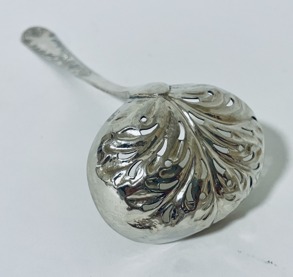A Georgian sterling silver sugar sifter spoon featuring a hand-pierced foliate bowl design and an engraved floral handle. View X