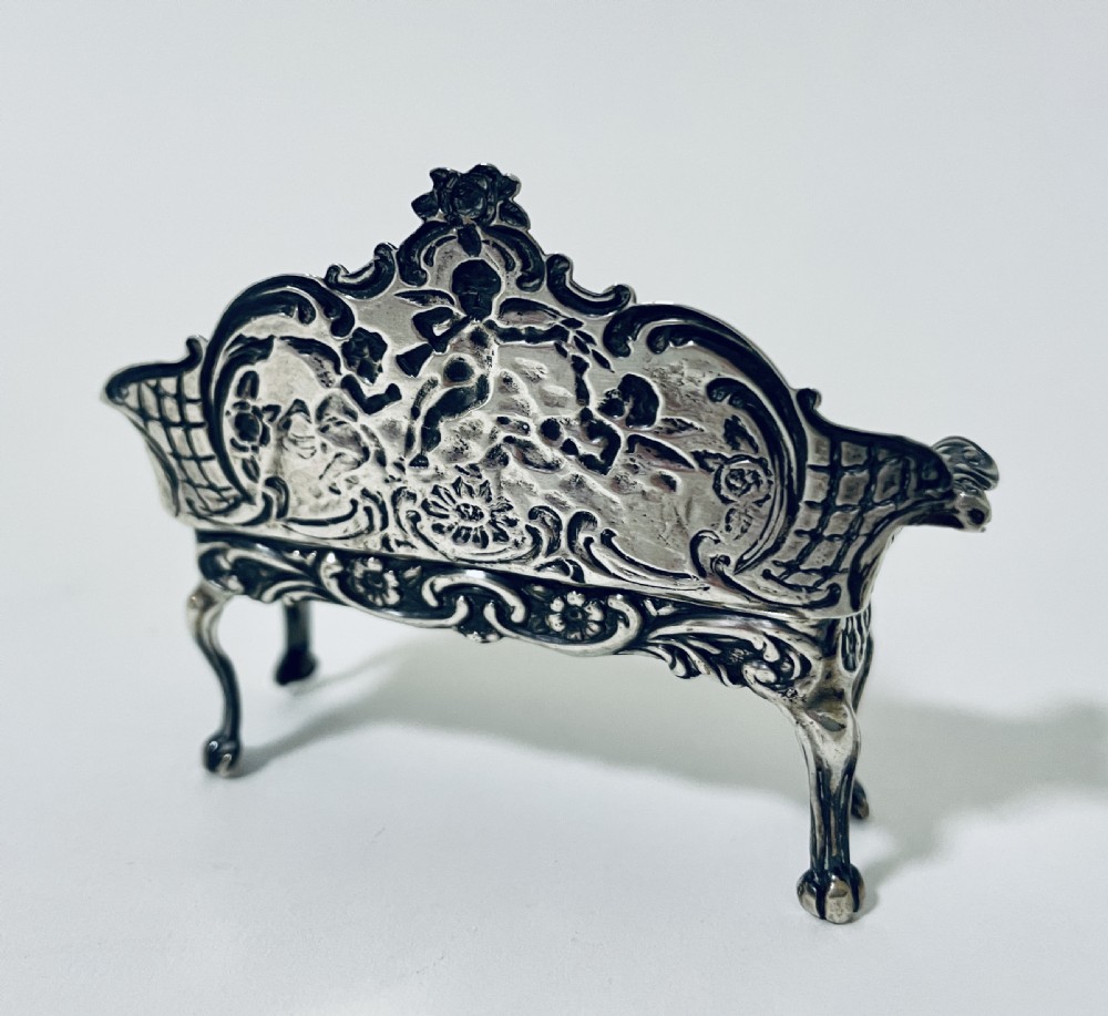An ornate miniature sterling silver sofa featuring embossed cherub motifs, scrollwork backrest, and cabriole legs. View VIII
