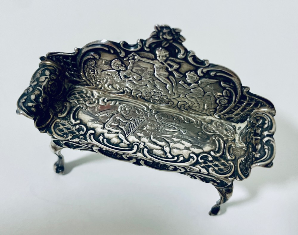 An ornate miniature sterling silver sofa featuring embossed cherub motifs, scrollwork backrest, and cabriole legs. View XII