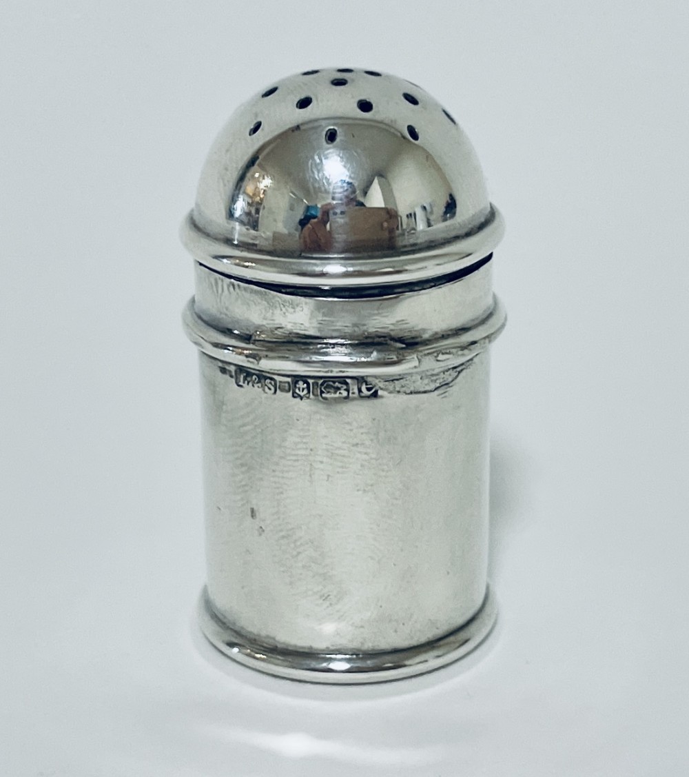 A small cylindrical sterling silver pepper pot featuring a domed perforated lid and visible stamped hallmarks on the upper body.