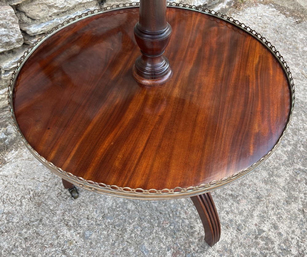 A Georgian dark mahogany two-tier dumb waiter featuring circular tops with pierced brass galleries, a central turned column, and sweeping reeded tripod legs on brass castors. View X