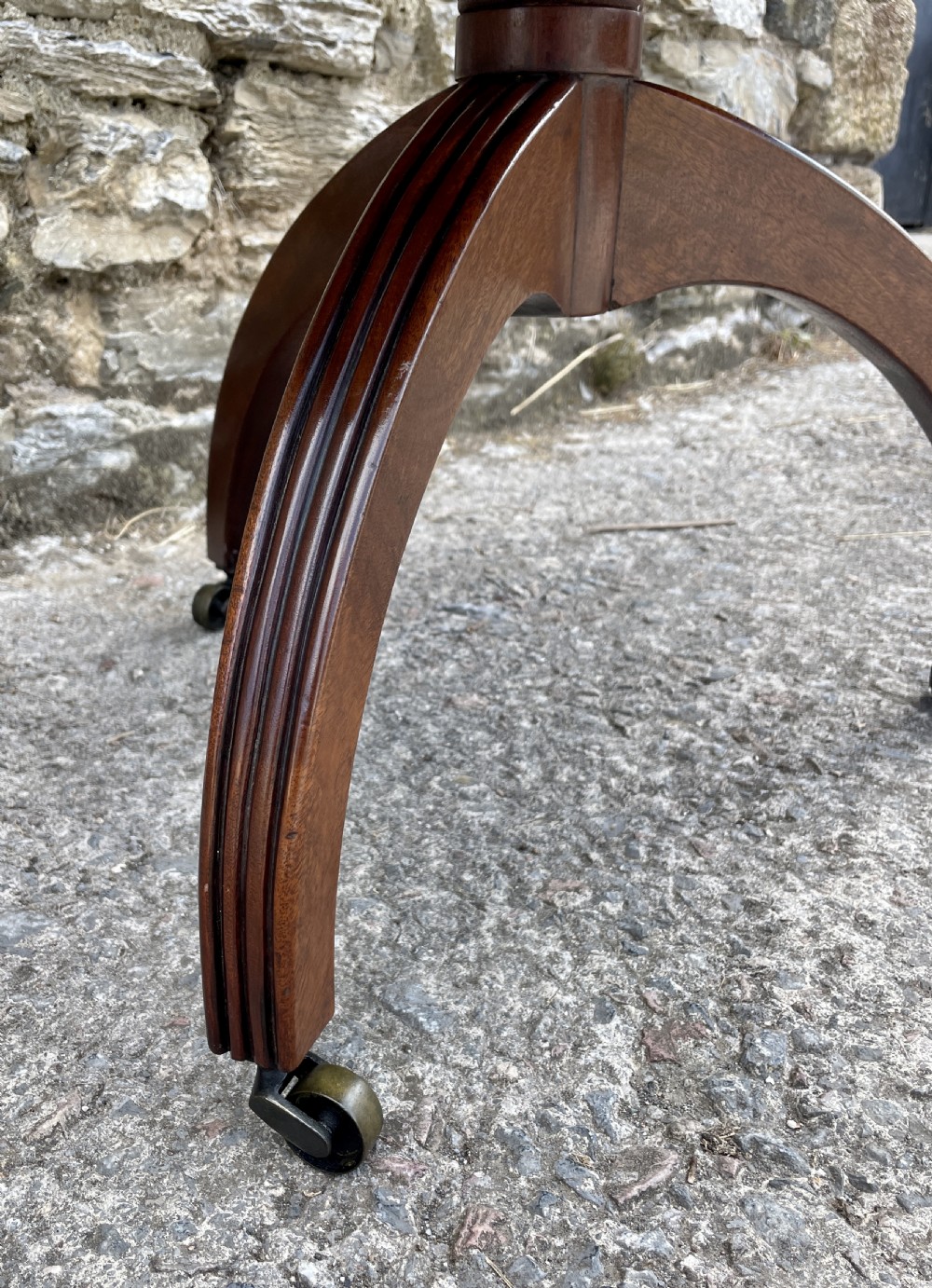 A Georgian dark mahogany two-tier dumb waiter featuring circular tops with pierced brass galleries, a central turned column, and sweeping reeded tripod legs on brass castors. View XVII