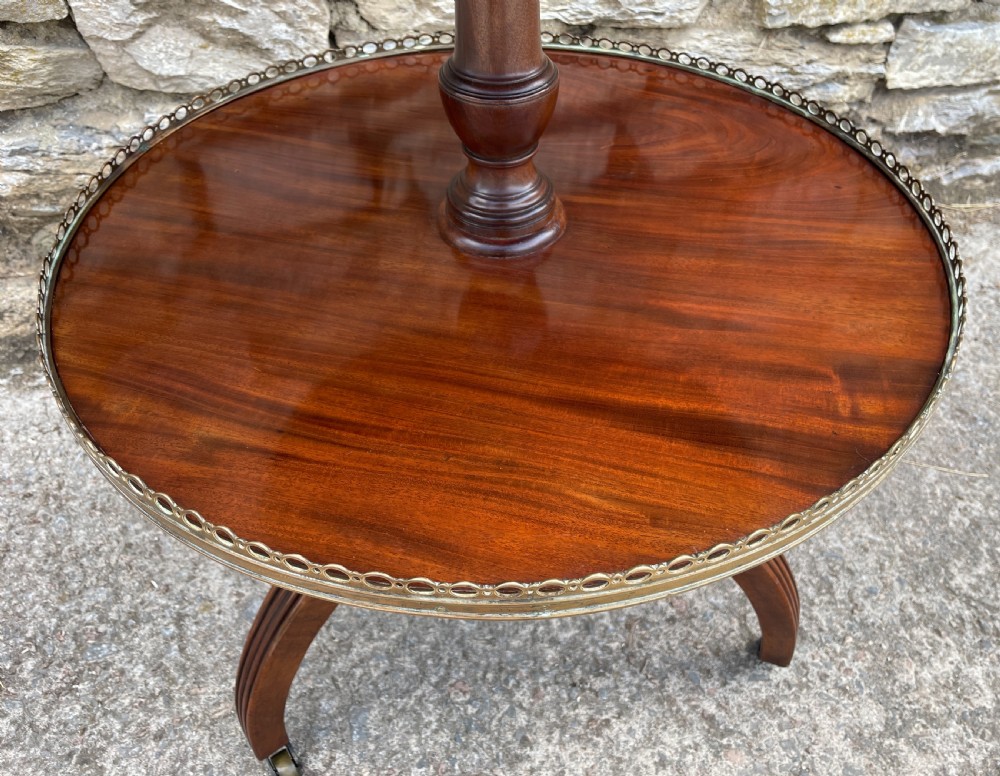 A Georgian dark mahogany two-tier dumb waiter featuring circular tops with pierced brass galleries, a central turned column, and sweeping reeded tripod legs on brass castors. View XX