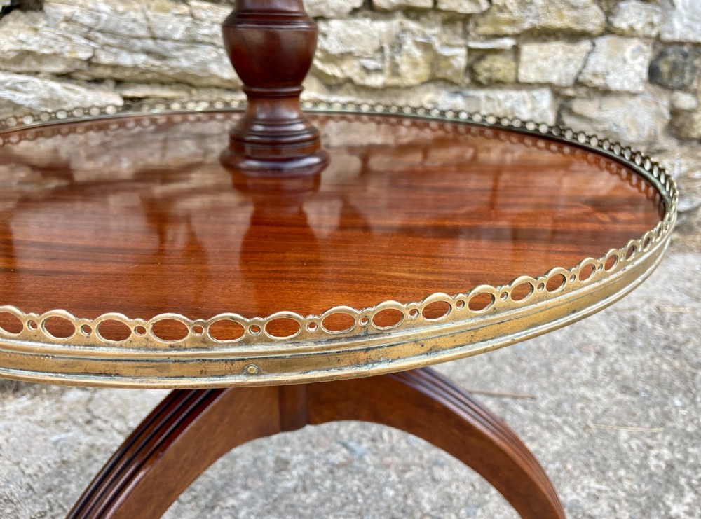 A Georgian dark mahogany two-tier dumb waiter featuring circular tops with pierced brass galleries, a central turned column, and sweeping reeded tripod legs on brass castors. View XXI