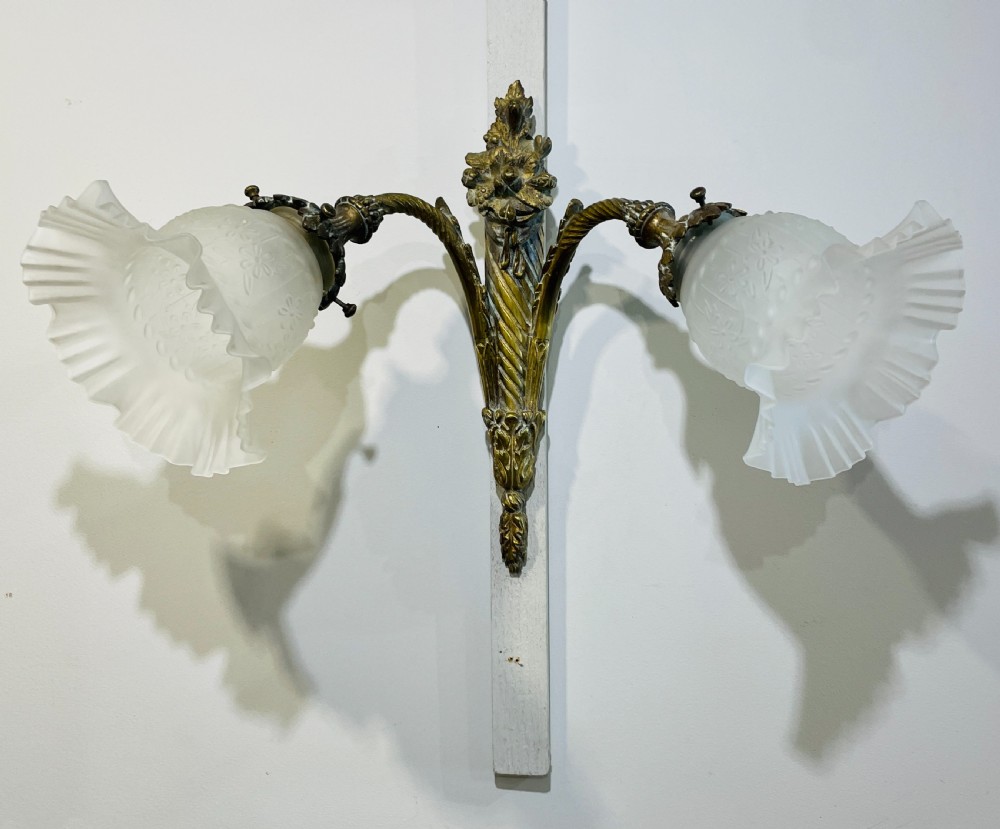 A Victorian twin-arm gilt brass wall sconce featuring reeded details, acanthus leaf motifs, and frosted frilled glass shades with etched floral patterns.