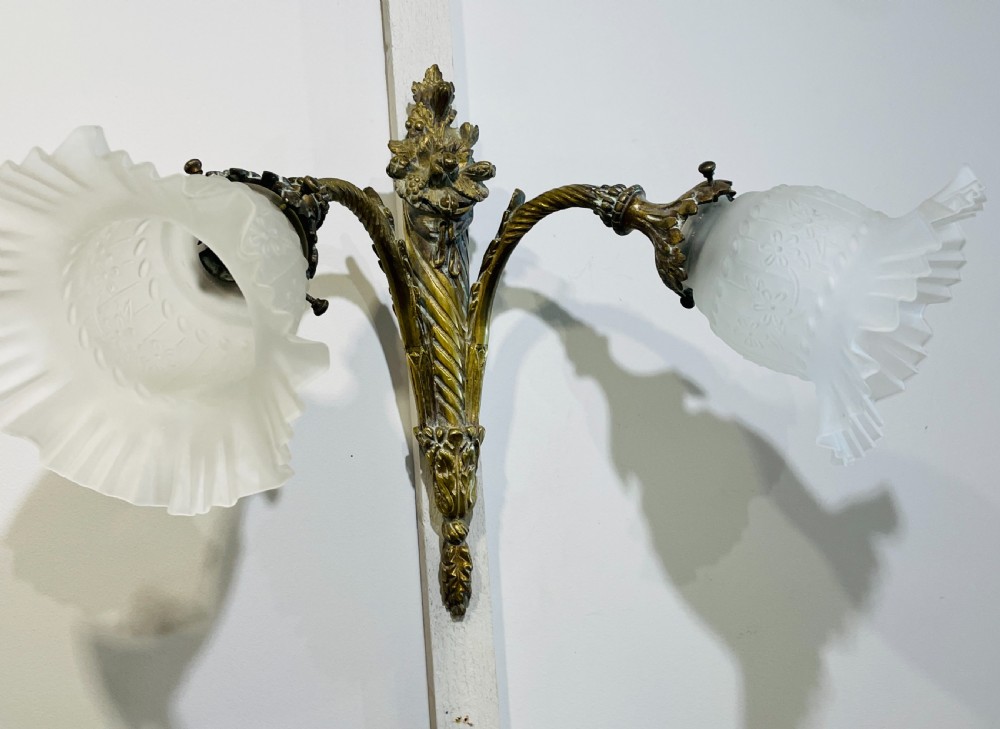 A Victorian twin-arm gilt brass wall sconce featuring reeded details, acanthus leaf motifs, and frosted frilled glass shades with etched floral patterns. View IV