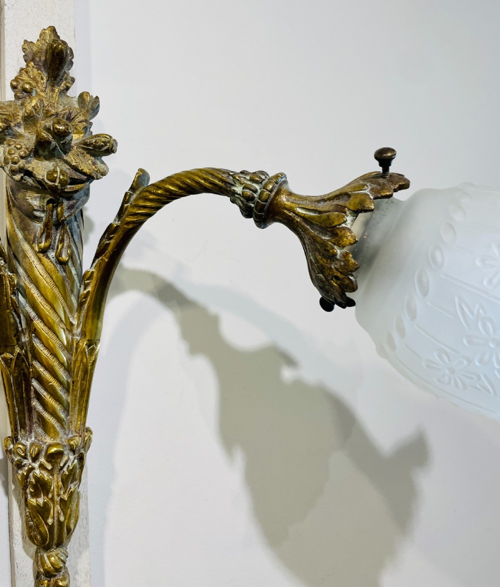 A Victorian twin-arm gilt brass wall sconce featuring reeded details, acanthus leaf motifs, and frosted frilled glass shades with etched floral patterns. View X