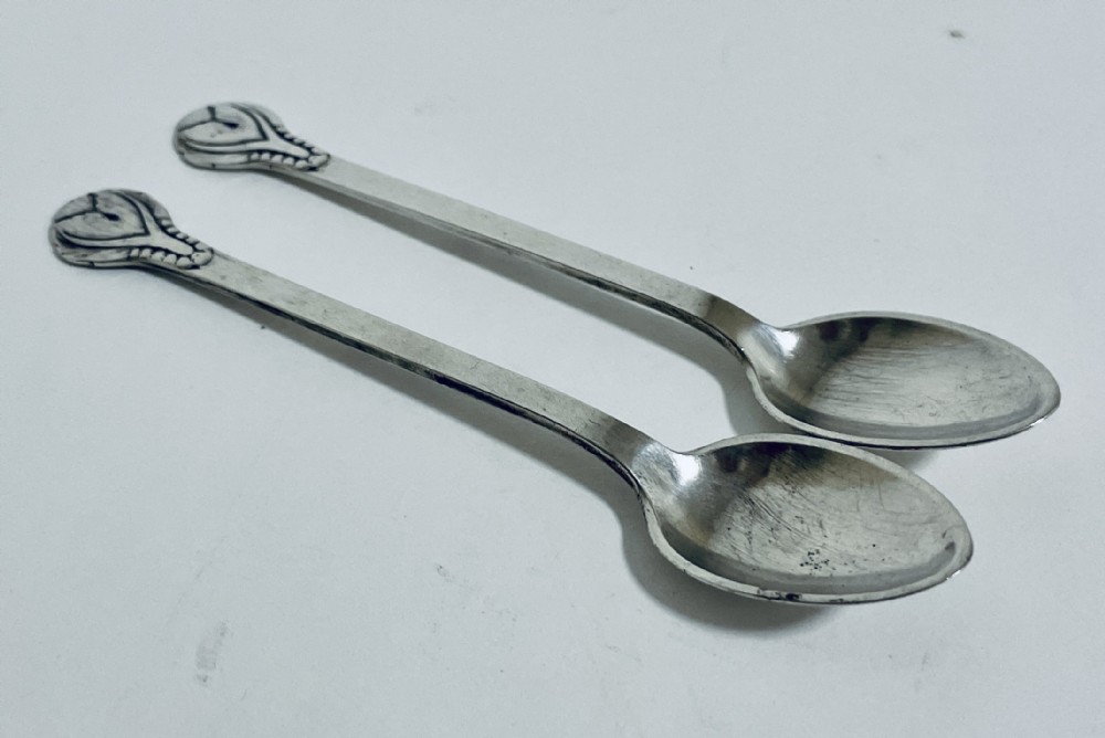 A pair of Danish silver teaspoons with stylised floral finials on the upper handles and oval bowls resting on a plain surface.