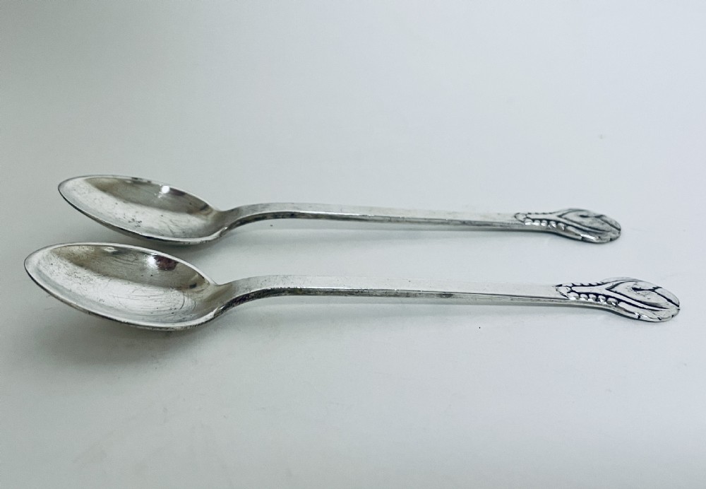 A pair of Danish silver teaspoons with stylised floral finials on the upper handles and oval bowls resting on a plain surface. View II