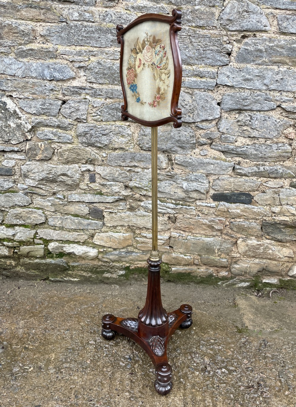 A Regency rosewood pole screen featuring a carved tripod base, adjustable brass rod, and a framed needlepoint panel with a floral wreath. View IX