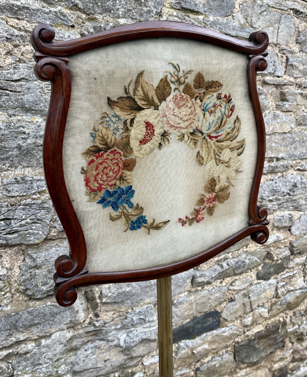 A Regency rosewood pole screen featuring a carved tripod base, adjustable brass rod, and a framed needlepoint panel with a floral wreath. View XVII