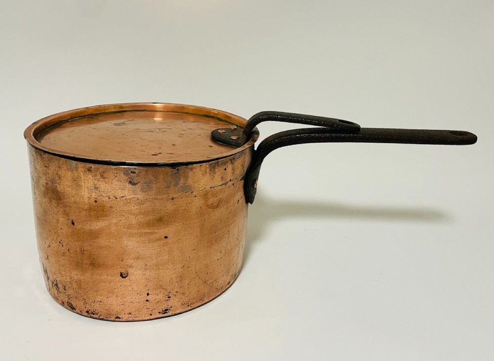 A large Victorian copper saucepan with a flat copper lid and a long dark cast iron handle.